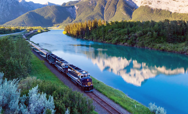 Image of a train winding through a lush valley surrounded by the Canadian Rockies